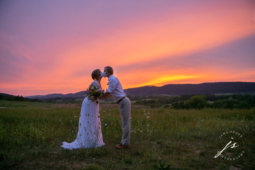 bride and groom kissing with masks on at sunset