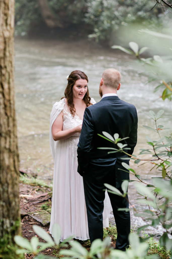 Bride smiles while reading vows to groom privately by a stream