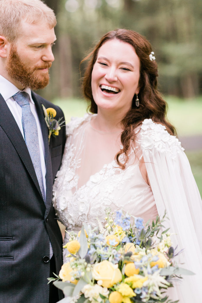 Bride is laughing while holding her bouquet near the groom