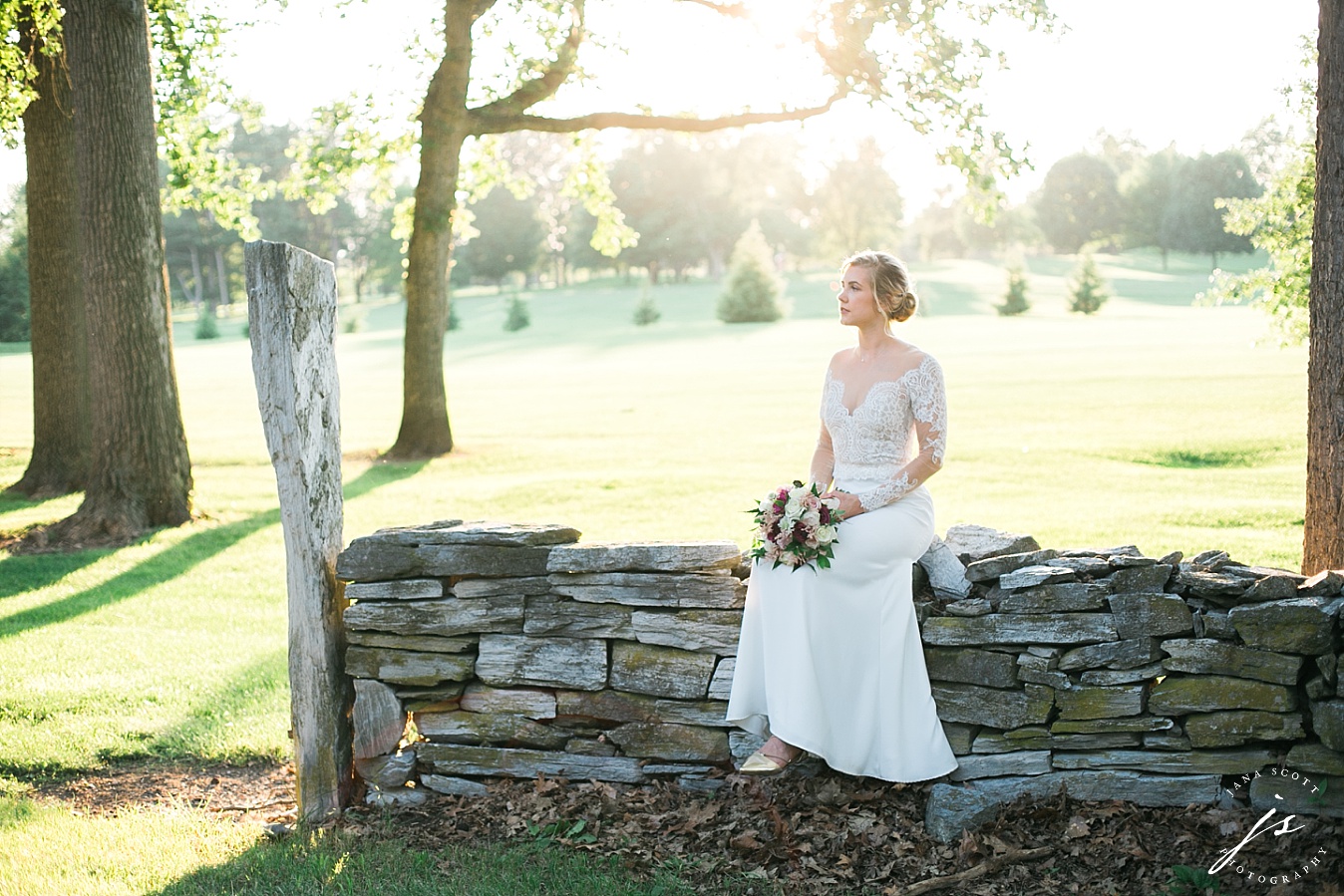 bride sits on a stone wall in evening light