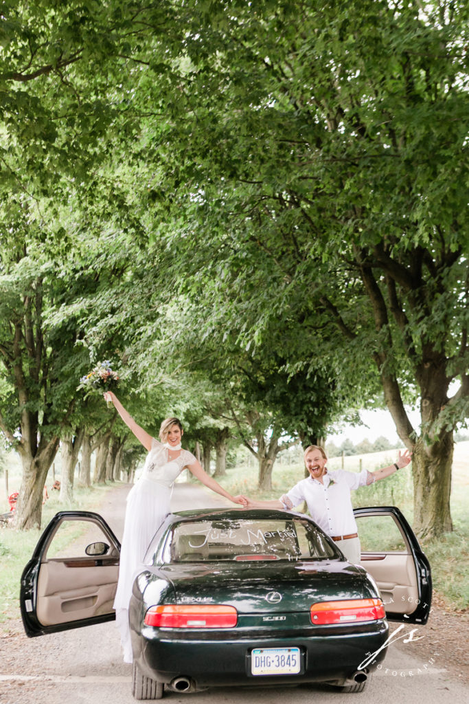 Bride and groom raising arms to celebrate while standing near car