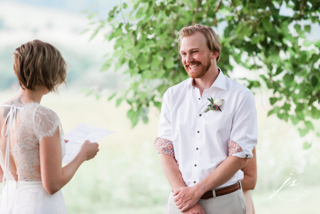 groom smiling at bride while she reads her vows