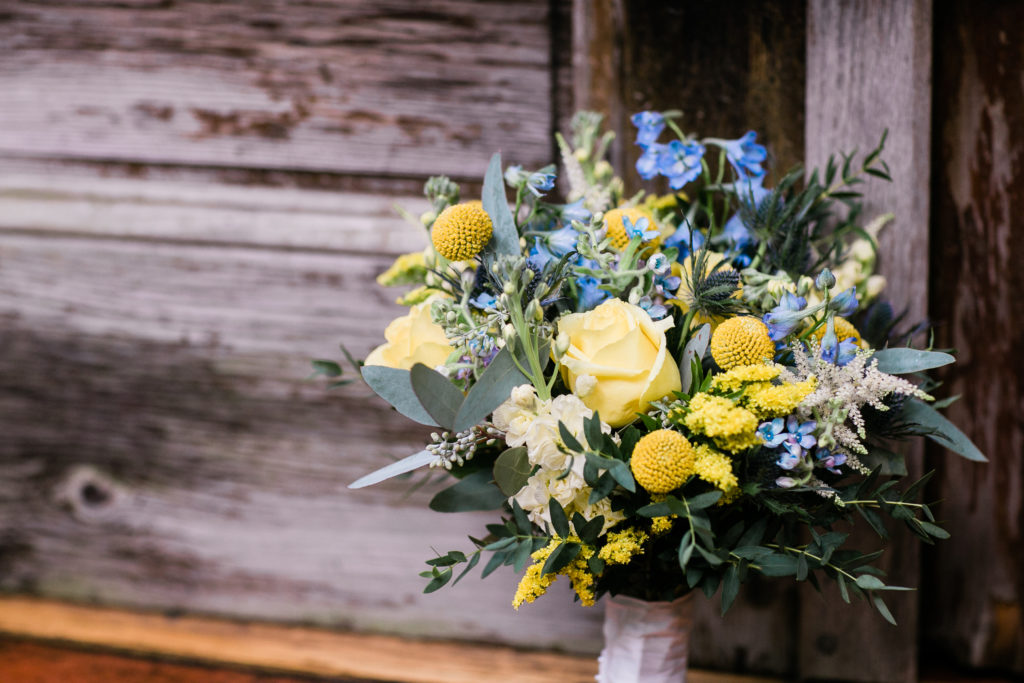 Yellow and blue flowers in a wedding bouquet leaning against a wooded door